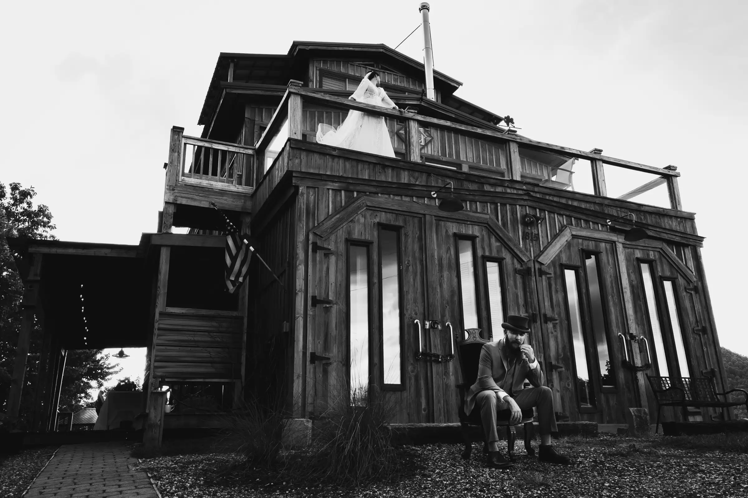Black and white of the bride on a high balcony while the groom sits below in a top hat