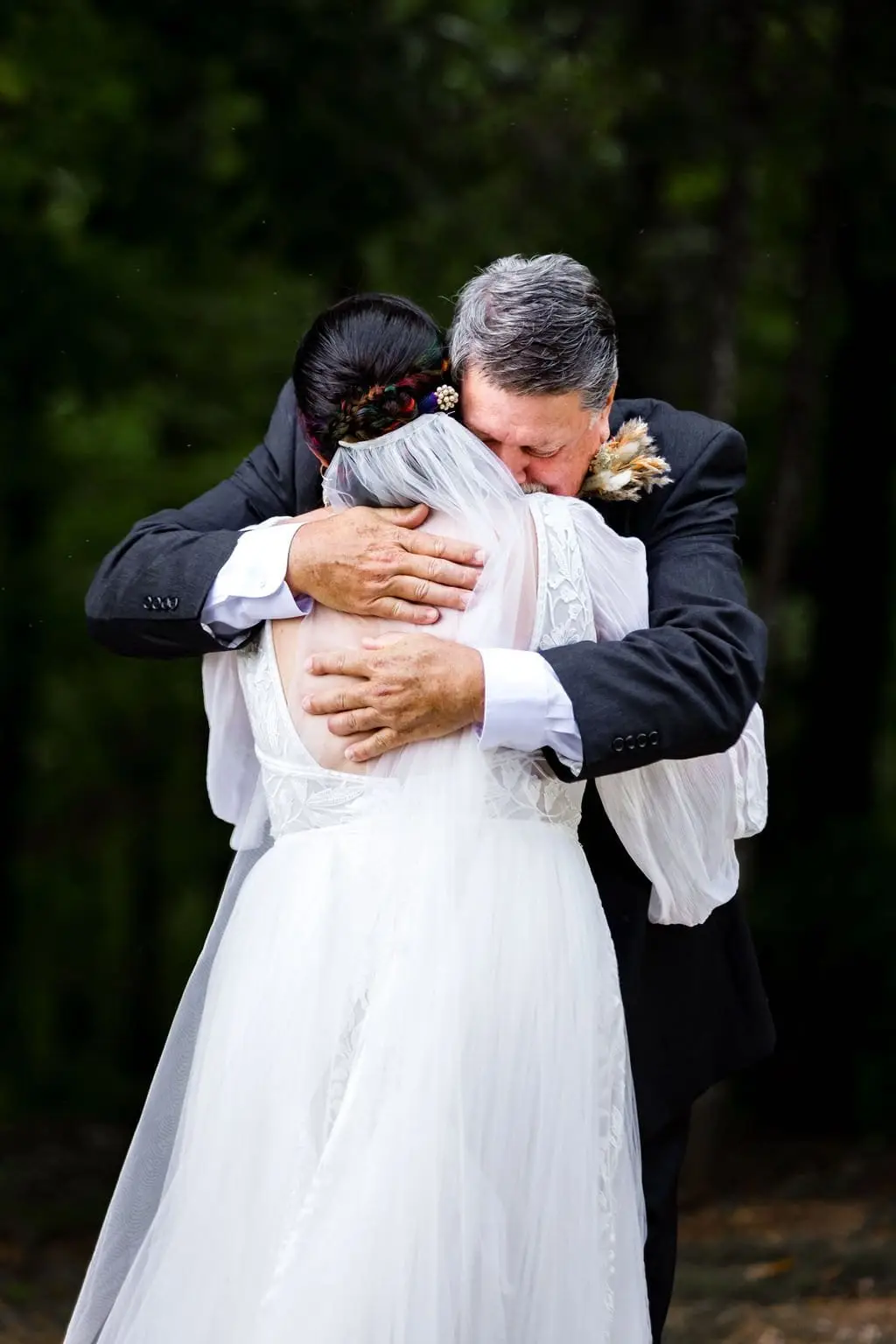 Bride in a long veil in a tearful hug with an older man in a dark suit before the ceremony
