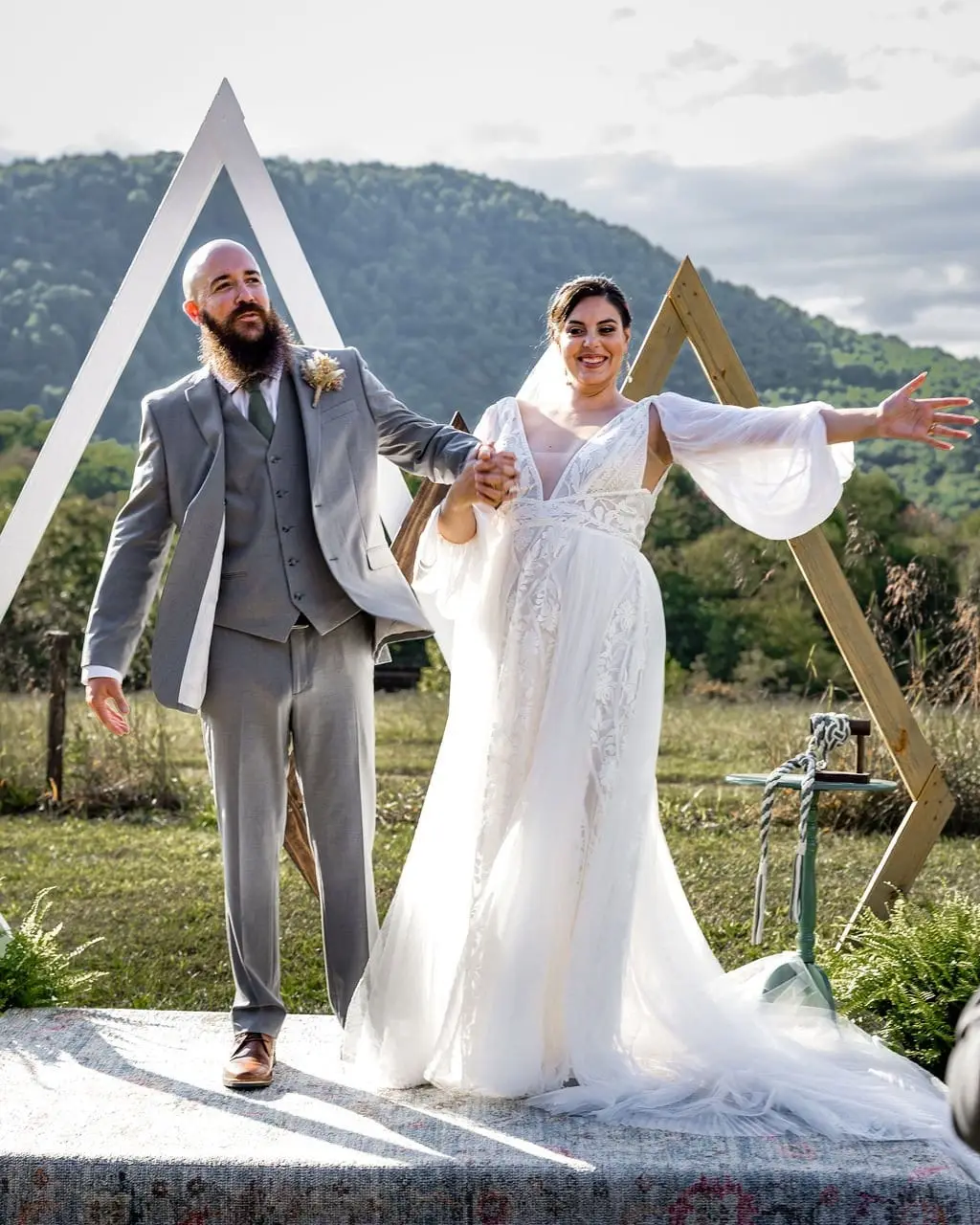 Bride and groom with arms outstretched celebrating on the ceremony platform with green hills behind