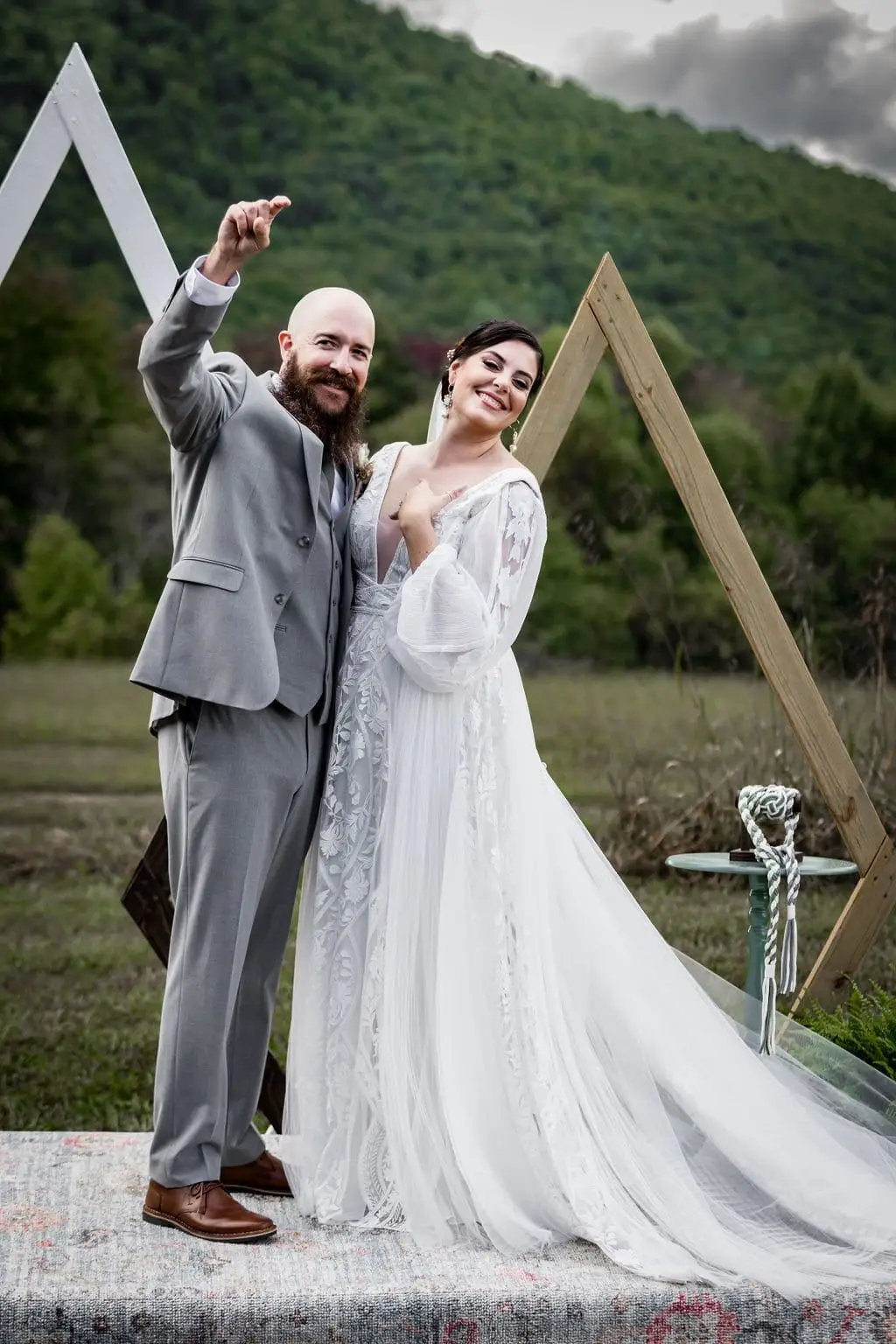 Groom raising a fist in celebration beside his smiling bride at the triangle arch