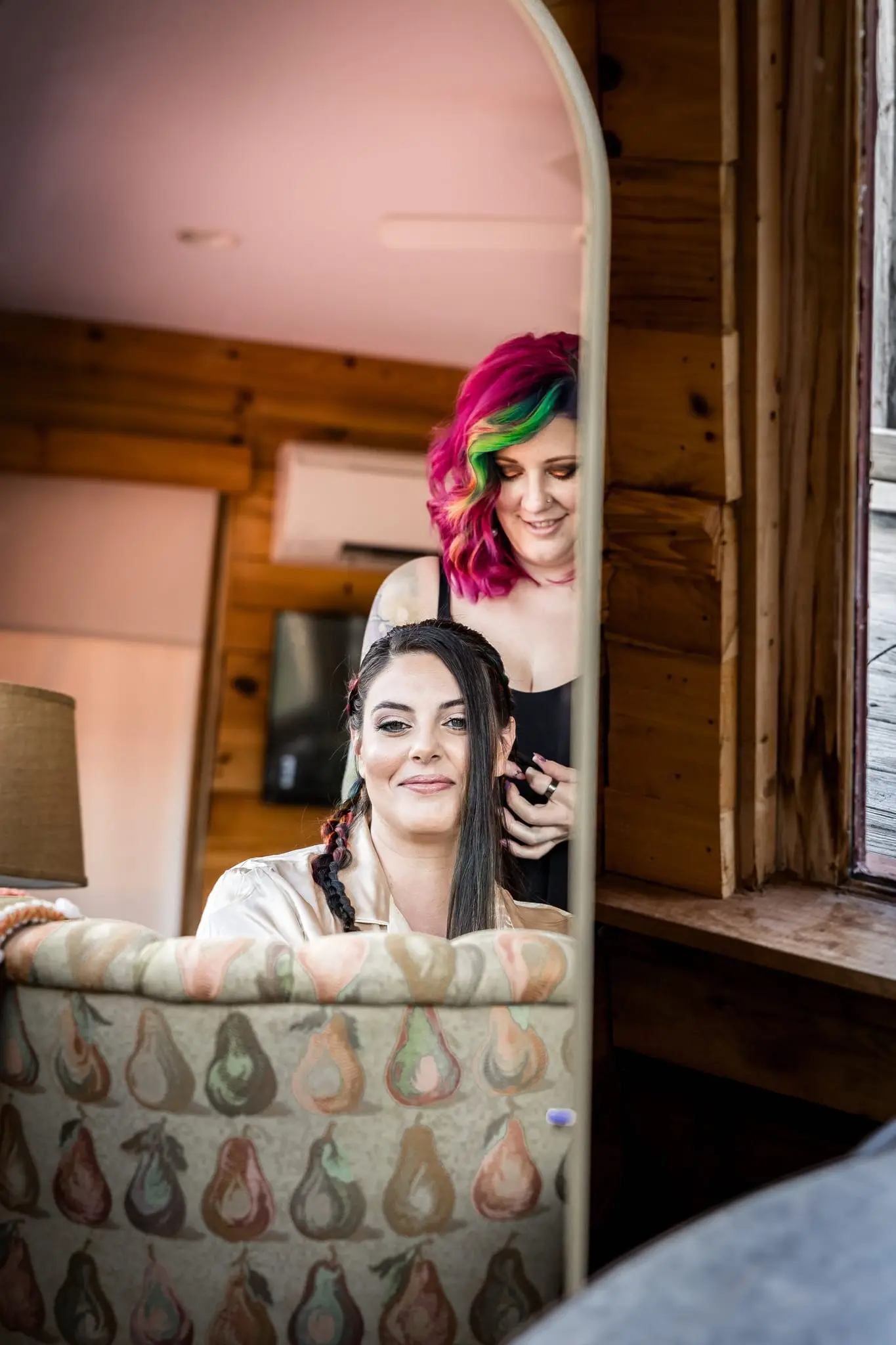 Bride smiling in a mirror reflection as her stylist with rainbow hair works on her hair