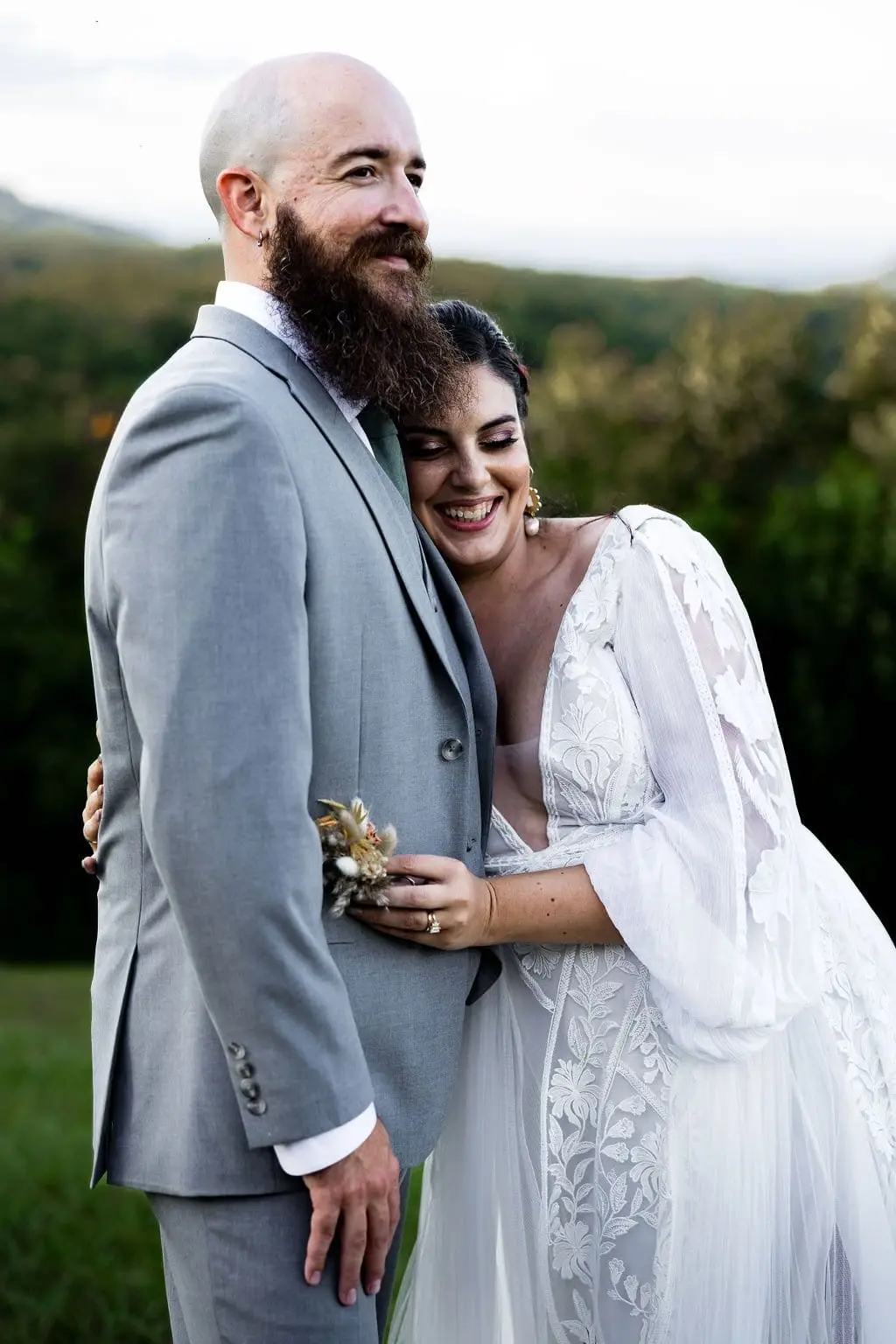 Groom grinning as the bride laughs and leans into his chest, a mountain ridge behind them
