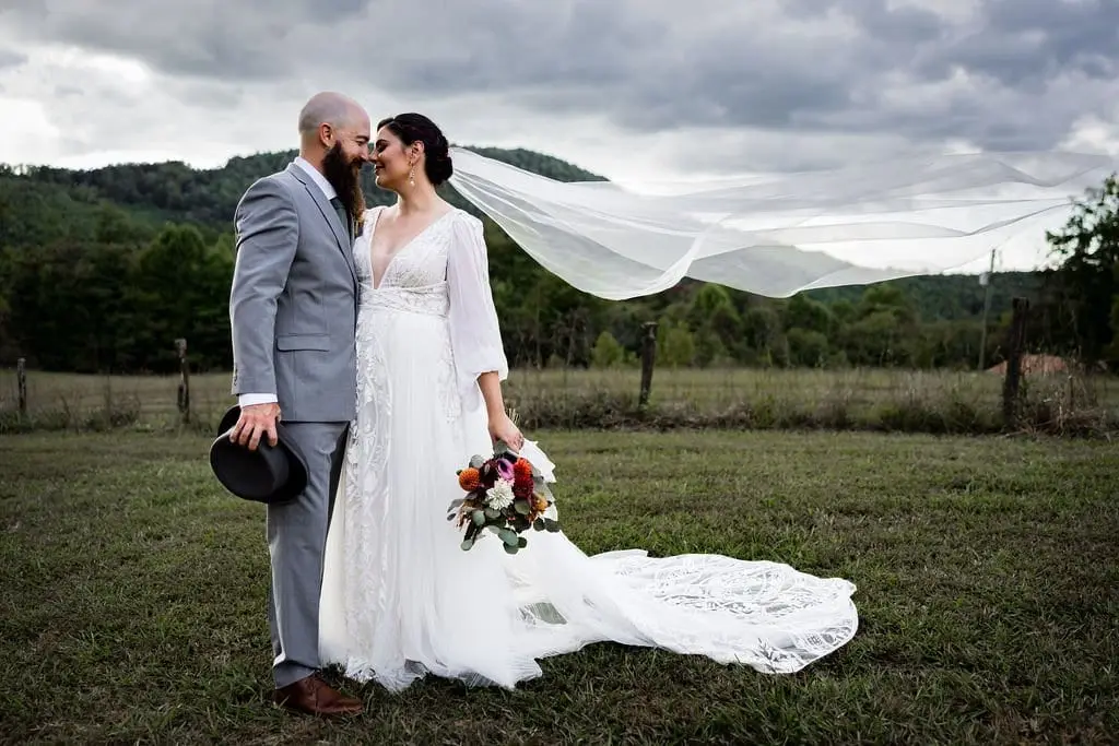 Megan and Brendan touching foreheads in a pasture while her veil streams behind under moody clouds