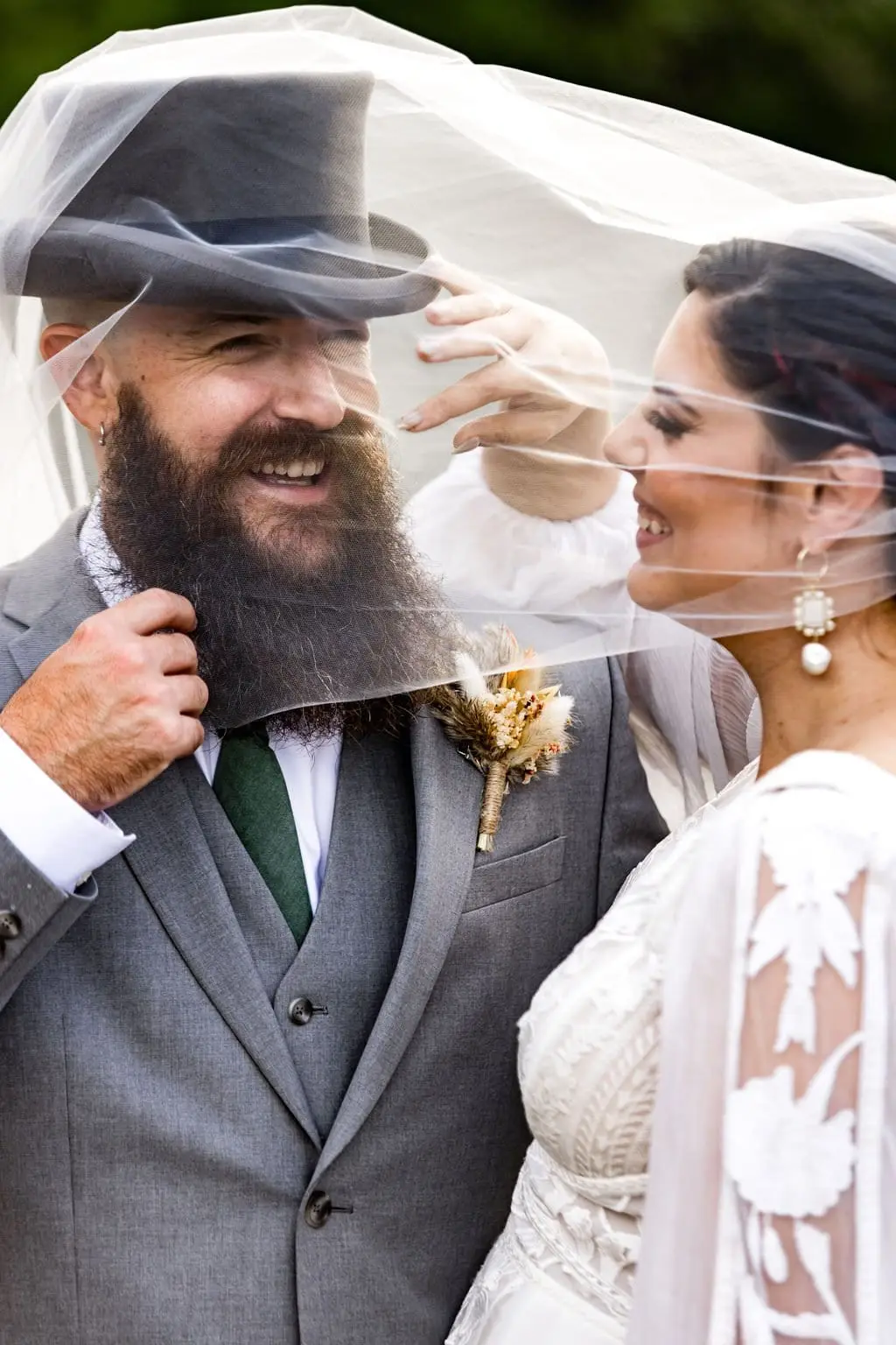 Megan and Brendan laughing together beneath her sheer veil, the groom in a top hat