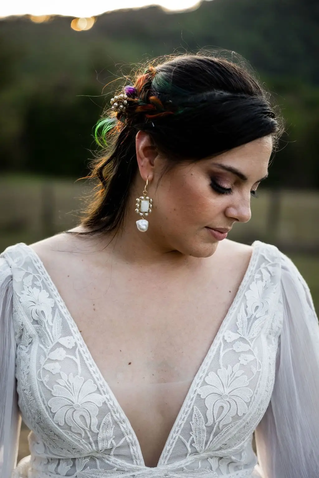 Close-up of the bride glancing down, with a pearl earring and rainbow-colored hair flowers