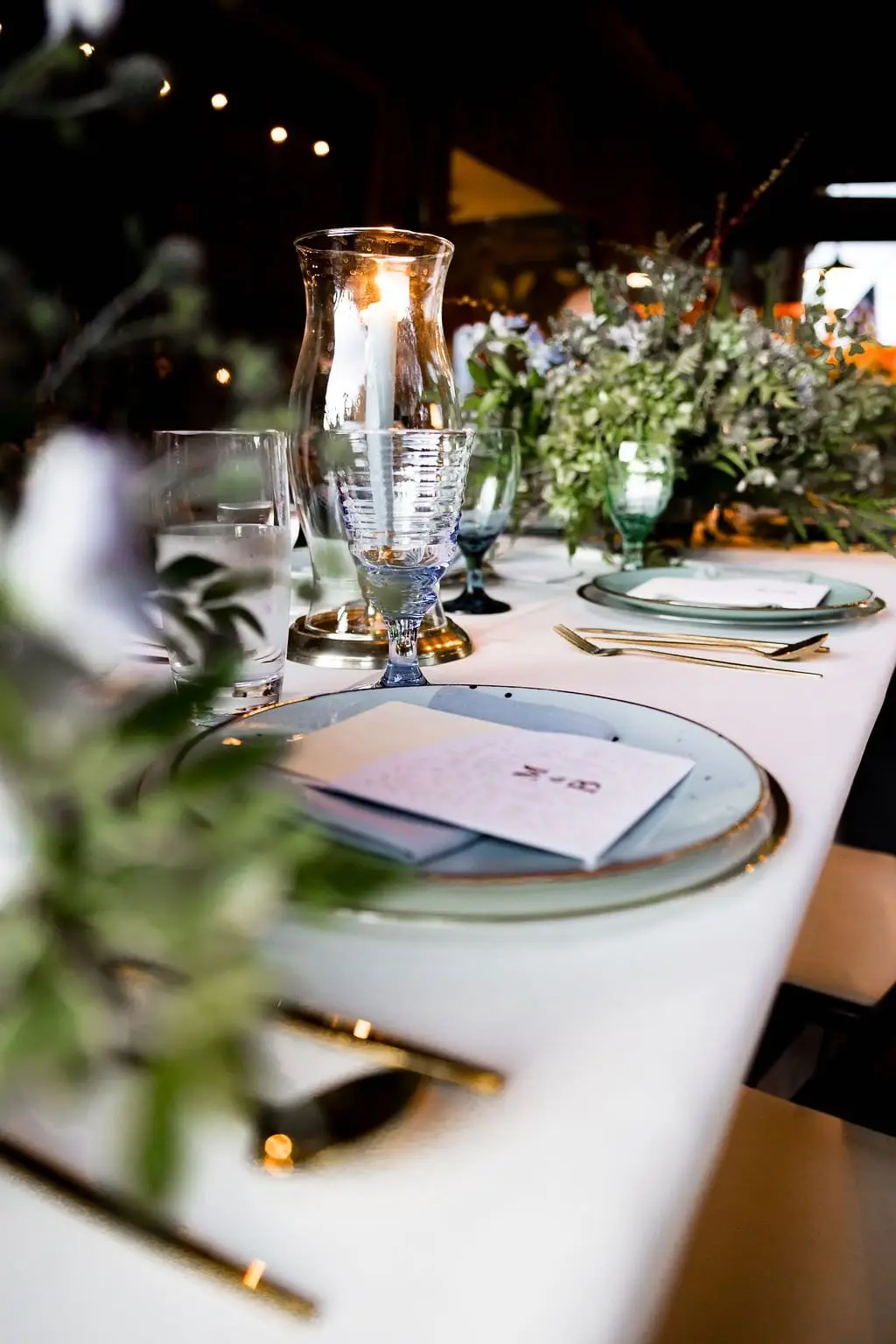 Place setting with a menu card, blue-green plates and gold flatware on the long reception table
