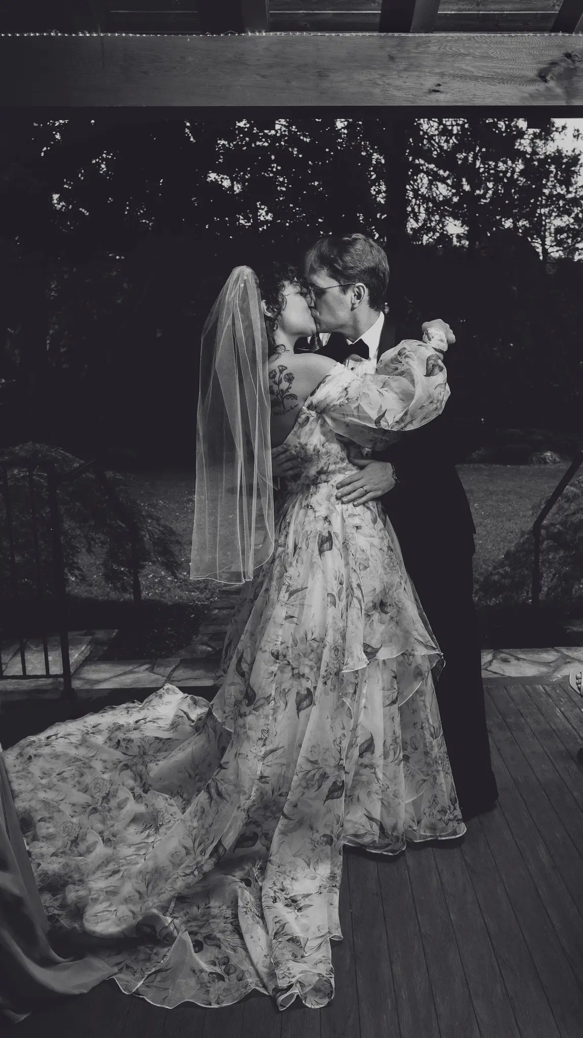 Black and white dip kiss on a wooden porch, the bride's veil and long floral train trailing
