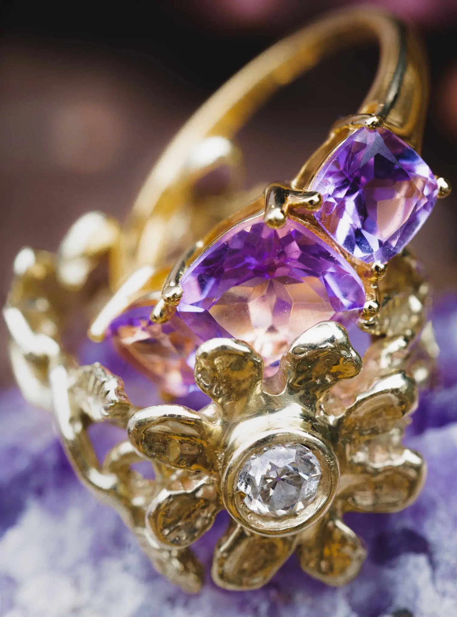 Close-up of a gold ring with amethyst stones and a central diamond on a purple geode
