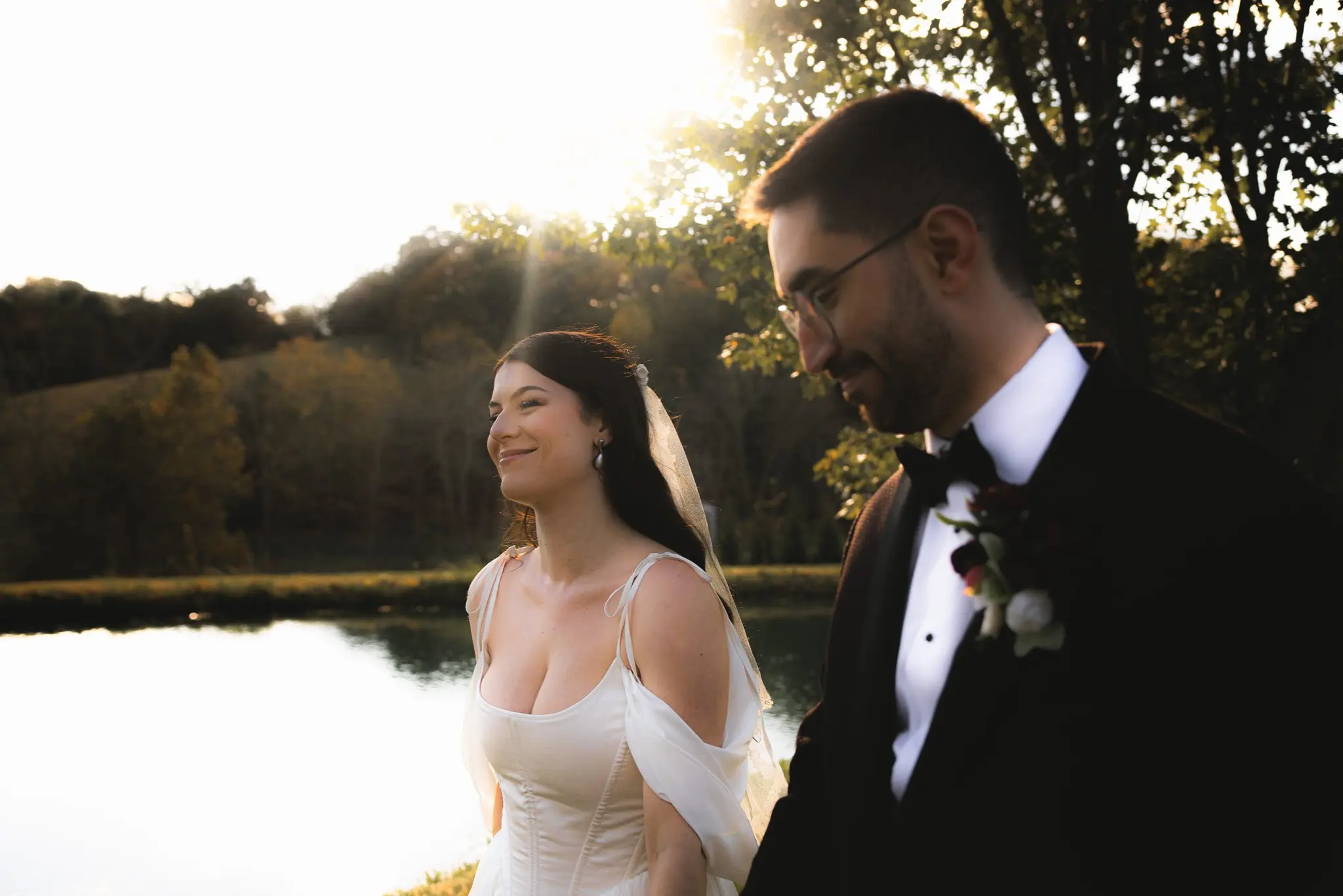 Bride smiling as the couple walk beside a pond in golden late-afternoon light