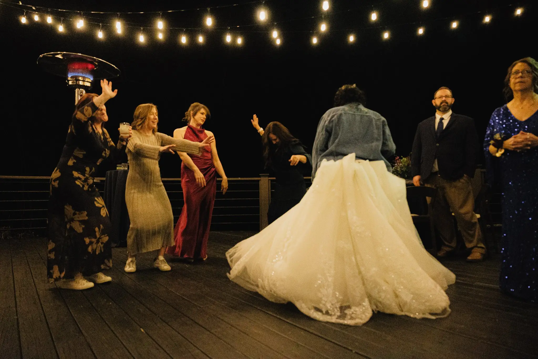 Bride twirling her ball gown with her friends on an outdoor dance floor under string lights