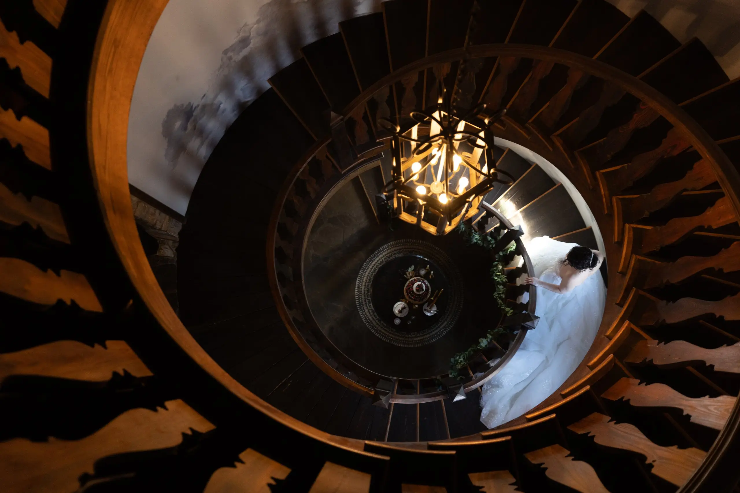 Looking straight down a spiral staircase at the bride under a glowing chandelier