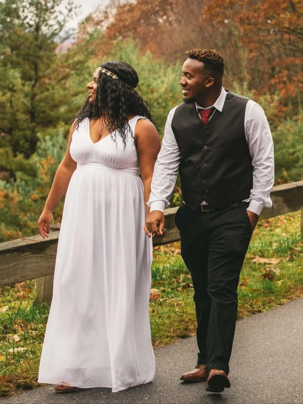 Dehja and Lance walking hand in hand along a path lined with autumn foliage